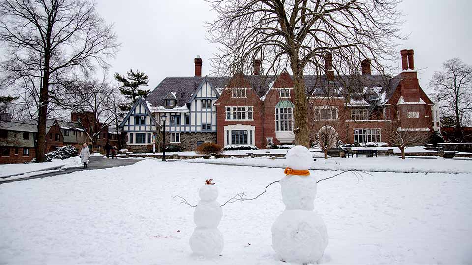 outdoor scene with two snow people in the foreground and large older building in the background